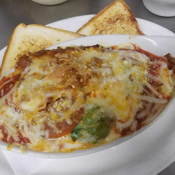 Baked lasagna with melted cheese and red sauce, served with two slices of toasted garlic bread.