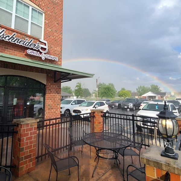 Reifschneiders Grill & Grape exterior with outdoor seating, a parking lot, and a rainbow in the sky.