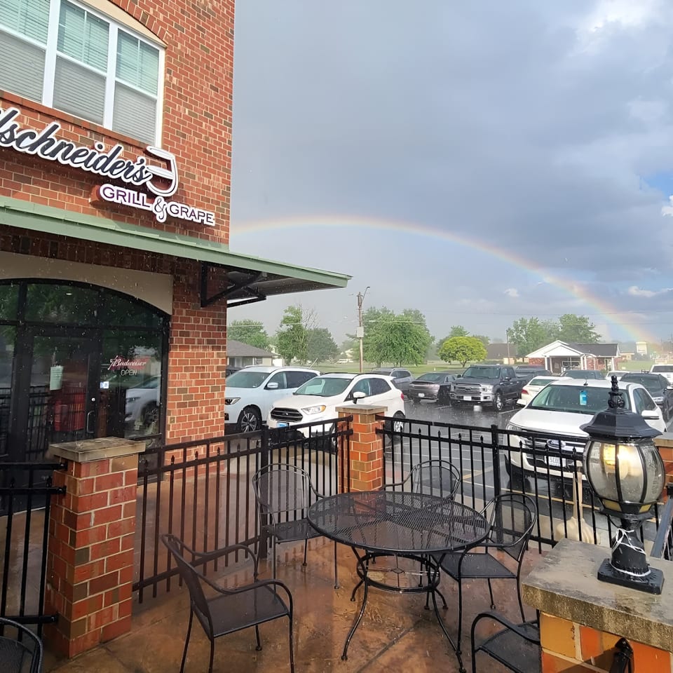 Reifschneiders Grill & Grape exterior with outdoor seating, a parking lot, and a rainbow in the sky.