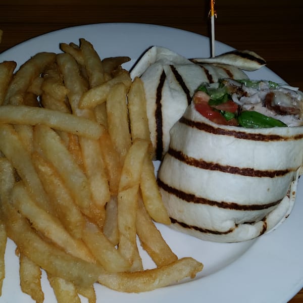 A grilled chicken wrap with tomatoes and lettuce, served with a side of golden french fries.