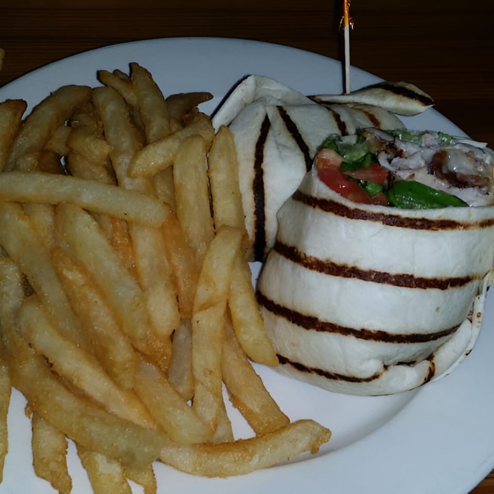 A grilled chicken wrap with tomatoes and lettuce, served with a side of golden french fries.