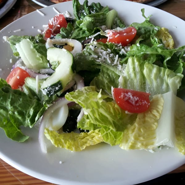 Fresh side salad with lettuce, tomatoes, cucumbers, red onion, and shredded cheese.