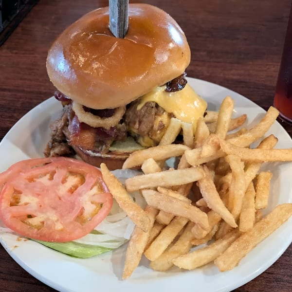 A Reifschneiders Grill and Grape burger with cheese, onion rings, and fries on a white plate.