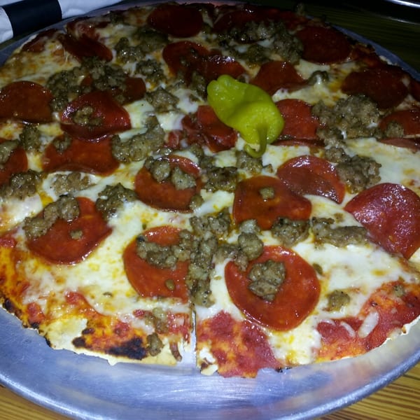 A Reifschneiders Grill and Grape pizza with pepperoni, sausage, and a green pepper on top.